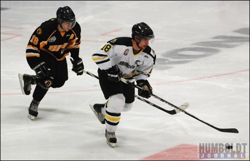 Gabe Minville (18) of the Humboldt Broncos brings the puck out of his end as he's chased by Mark Cross of the Estevan Bruins.