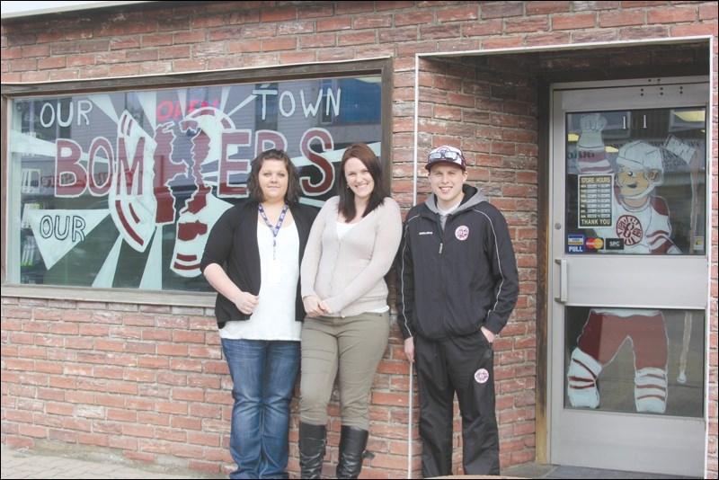 Carissa Mason (left) and Amanda Badgero were two of three artists at MTS Communication responsible for the store window’s Bomber burst and the door’s hockey player for the business-decorating contest. Flin Flon Bomber assistant coach Gary Childerhose presented the artists and MTS Communications with tickets to last night’s game. Missing from the picture is artist Nicole Lysohirka. Businesses in the Flin Flon area showed their support for the Bombers with window paintings and other decorations. The Bombers hosted the Notre Dame Hounds last night in game three of the series and will look to secure a win in game four tonight at the Whitney Forum.