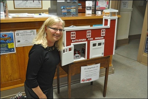 Curator of the Fred Light Museum Bernie Leslie with this year’s raffle project, a dollhouse version of the 1905 replica fire hall that makes up part of the museum complex. Made and donated by the museum board chair Floyd Anderson, the dollhouse draw will be made in December.