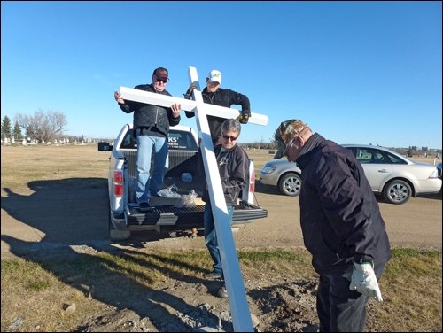 Knights of Columbus Father Bigonesse Council 5626 Grand Knight Tom Sieben and Garret Francais stand on the back of a truck to raise a new cross at the Battleford Cemetery while Howard Senger guides the base. Project co-ordinator Ron Sack makes sure the bolts fit. Photos submitted
