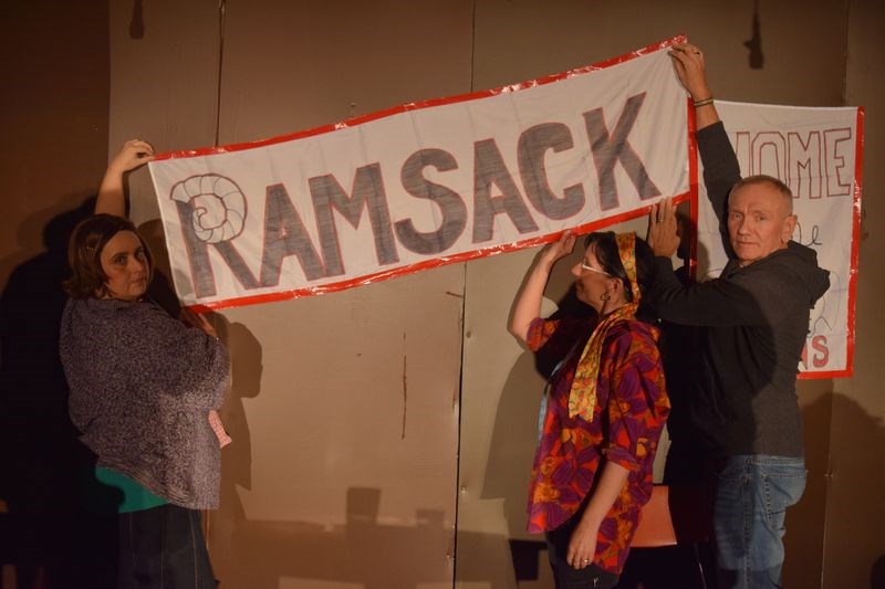 Placing the “Ramsack” banner on the rear wall of the stage during the Death and Taxes dress rehearsal last week, from left, were: Nikki Larson, who portrayed Lydia Kleft; Annett Purchase, who was Evelyn Martindale, and Jack Koreluik, the director of the play.