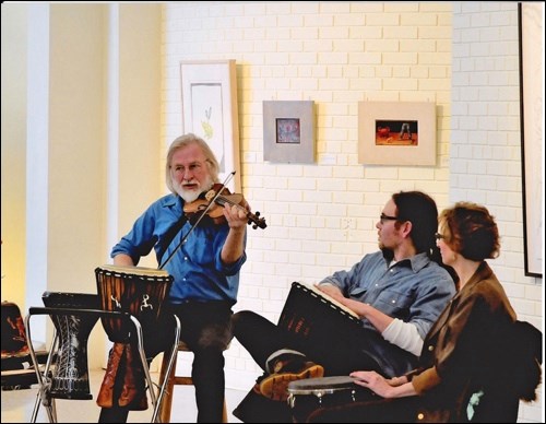 Keith Bartlett playing fiddle behind djembe drums at the Chapel Gallery in North Battleford. Photo by Jim Taylor