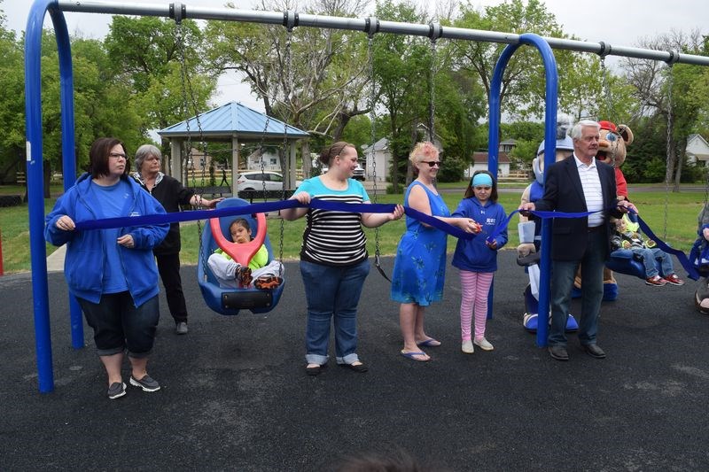 In front of the swings at Sparty Park on Friday, Leah Schwartz cut a ribbon that was held by, from left, Kendra Simon, Alana Smutt, Shelley Filipchuk and Mayor Rod Gardner.