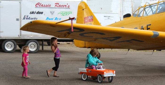 Young attendees enjoy a vintage pedal car keeping dry under the wing of a cropduster.