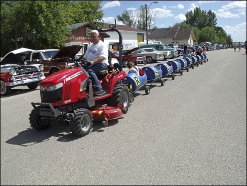 David Ruzesky pulling the kids around on Radisson's barrel train, with the street behind lined with vintage vehicles.