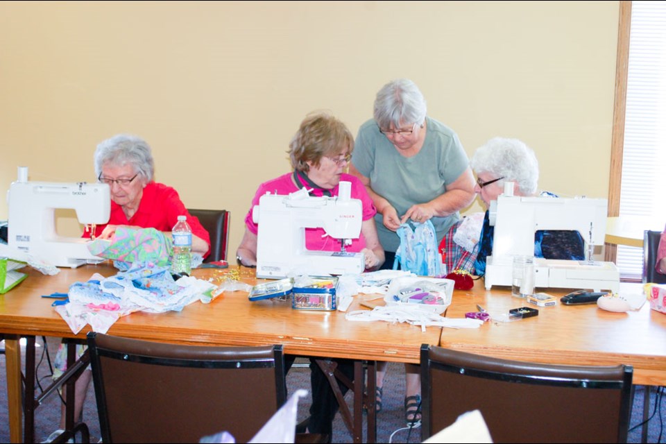 Linda Hanson checks some button sewing work with Carol Barrett (left) and Rita Bezaire.