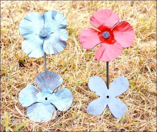 The creation of the steel, memorial poppies is displayed in this photograph. Clockwise from the bottom right: the blank cut from steel plate; a forged, hammered poppy; a poppy with stem and stamen added; and the finished painted product.