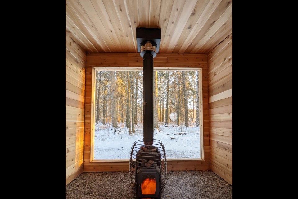 Inside a wooden sauna with a fire blazing and a snow-topped forest out the floor-to-ceiling window. / Glamp Good | Facebook
