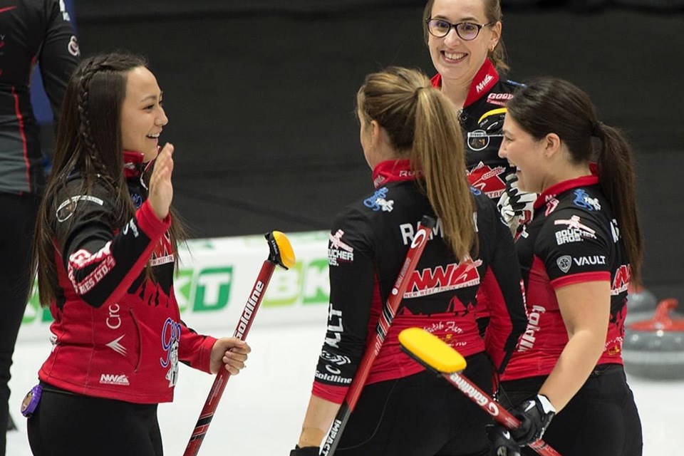 Four women on a curling team in matching jerseys high five and celebrate with brooms in hand. / Curling Alberta | Facebook