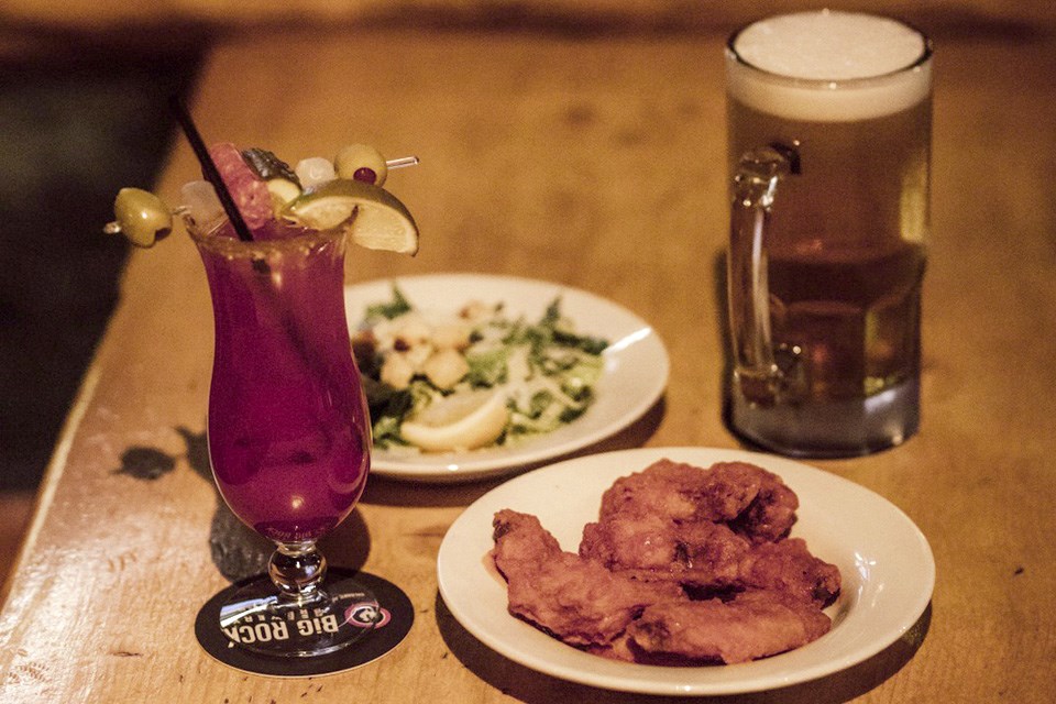 A table featuring a plate of chicken wings, a salad, a pint of beer, and a cocktail at Ralph's Texas Bar & Steak House. / Ralph's Texas Bar & Steak House | Facebook