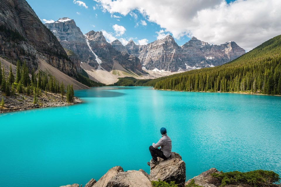 Lake Louise: A man sits on a rock overlooking Lake Louise with bright, turquoise water in front of him / Fairmont Chateau Lake Louise
