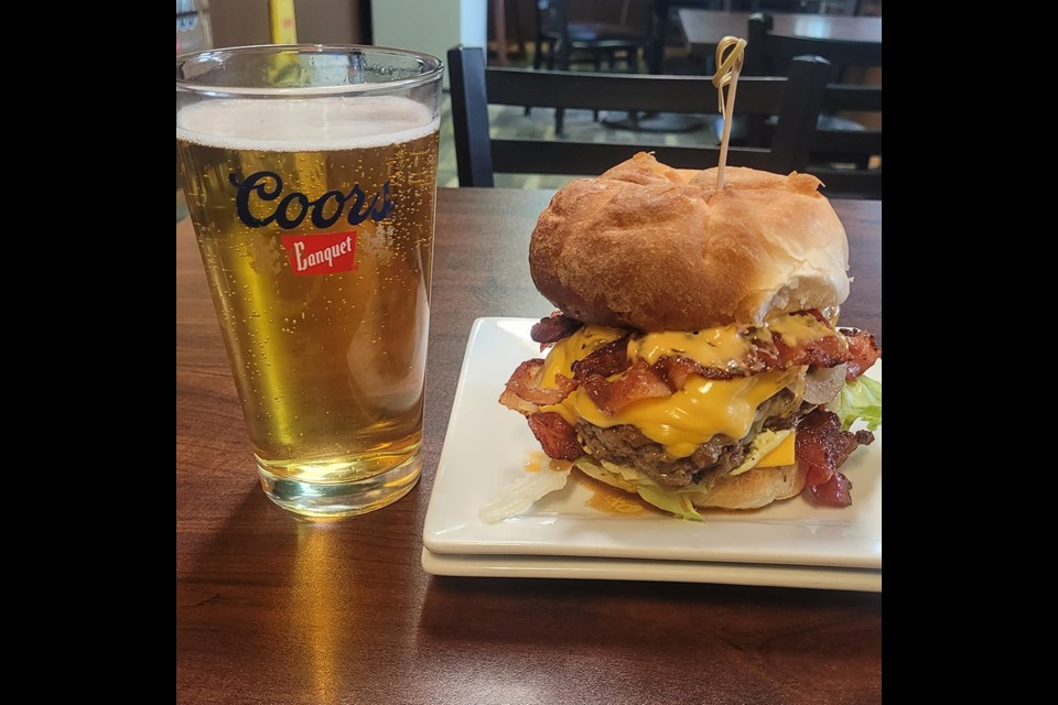 A big double burger exploding with toppings next to a pint at Fireside Hwy 41 Roadhouse Bar And Grill in Czar, Alberta / Fireside Hwy 41 Roadhouse Bar And Grill | Facebook