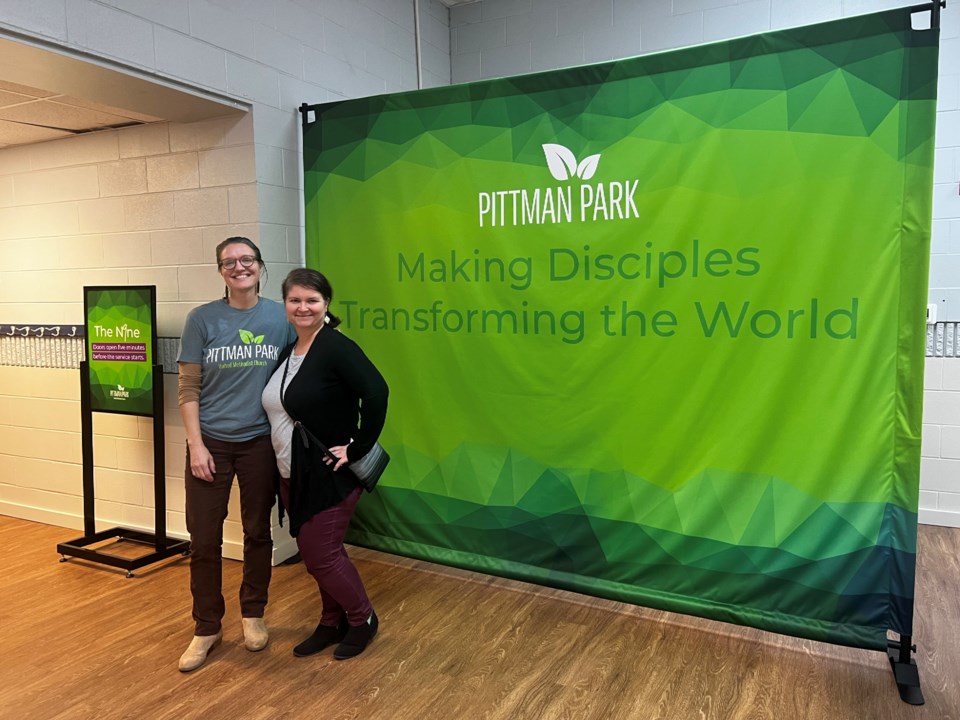 Image of Pittman Park Children's Director Megan Hopkins and church congregation member Michele Martin in front of a green church sign