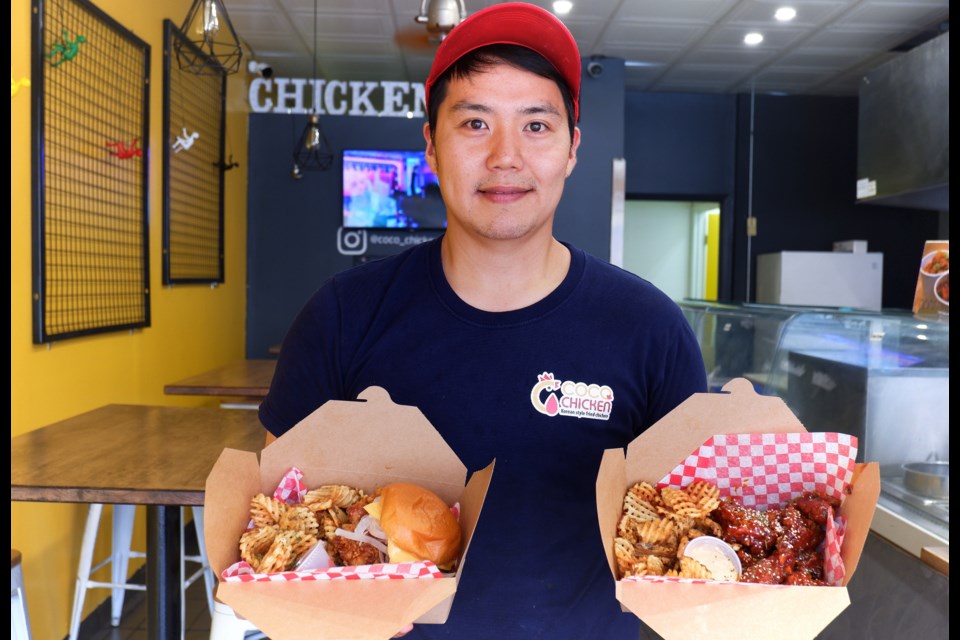Owner Minkyo Seo holds a box of fried chicken burger with waffle fries and a box of chicken wings with waffle fries in his restaurant. Anam Khan/GuelphToday