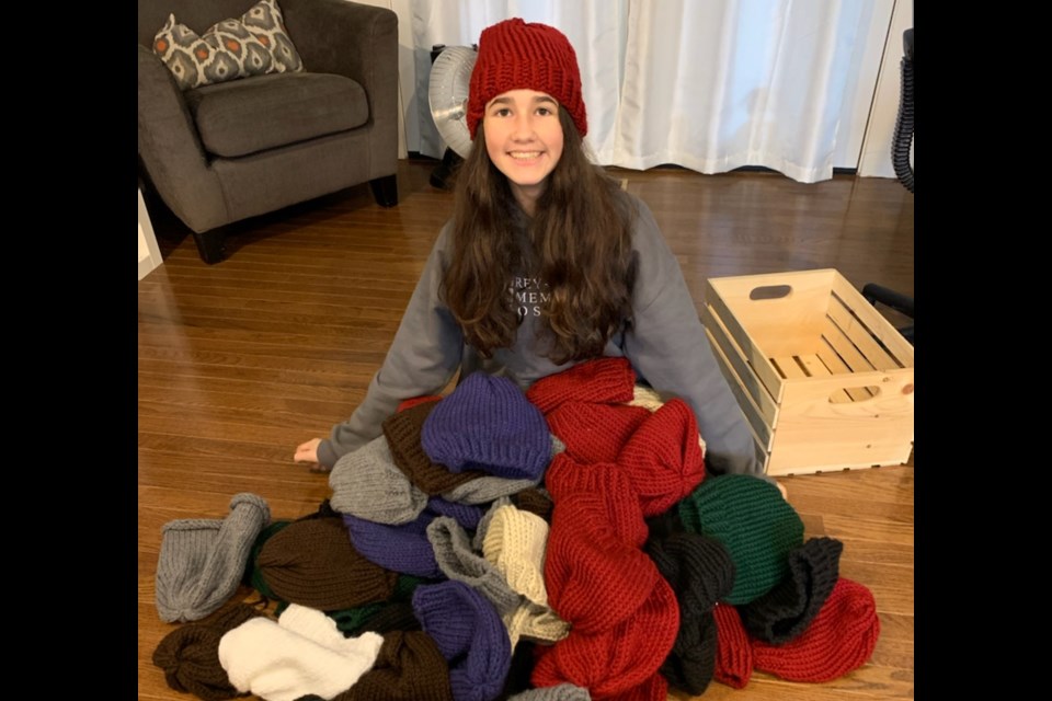14-year-old Colby Tufford sits with dozens of toques she knit during the pandemic. Supplied photo