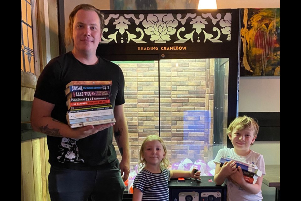Brandon Rennie stands in front of the 'Reading Cranebow' holding books with his children, Amelia Rennie and Oliver Rennie. Supplied photo