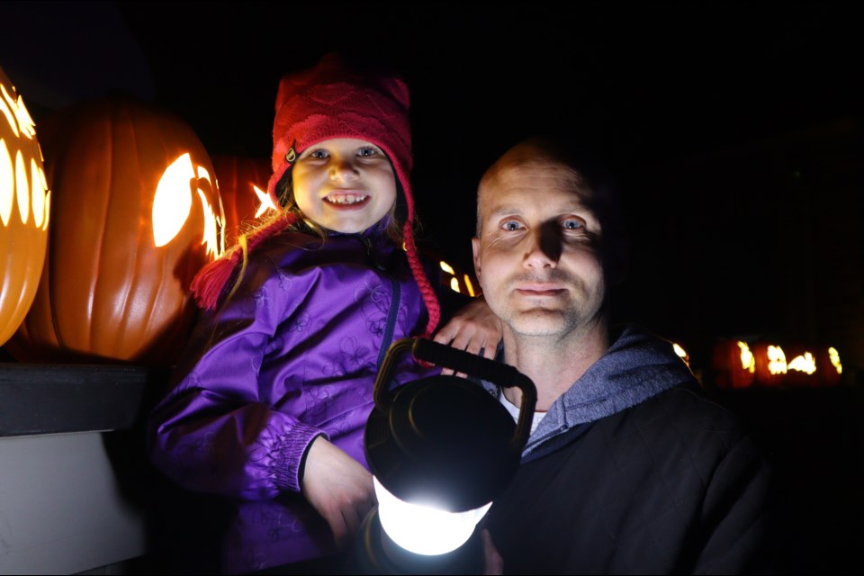 Shawn Gusz and his daughter pose in front of a line of pumpkins.