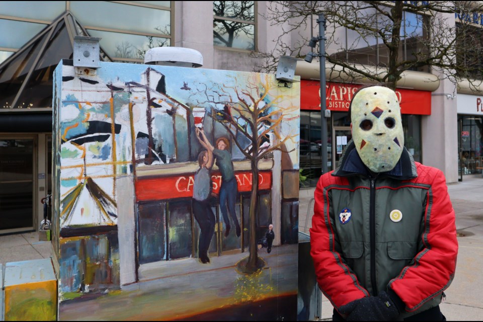 Artist Eric Kirkwood who says he doesn't like the way his face looks in photos, poses beside one of his works in a homemade mask. 