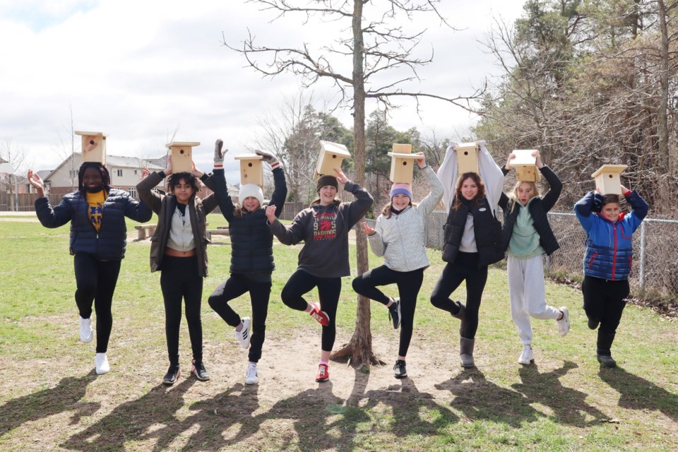 St. Ignatius students holding their birdhouses while standing in a tree pose