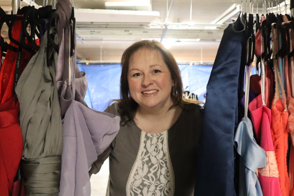 Carla Holmes, Princess Project Guelph coordinator peaking her head through a clothing rack of dresses.