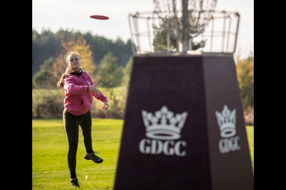 Paulina Ciolko throwing a disc into the basket at the Guelph Disc Golf Club at Victoria Park Valley Golf Club.
