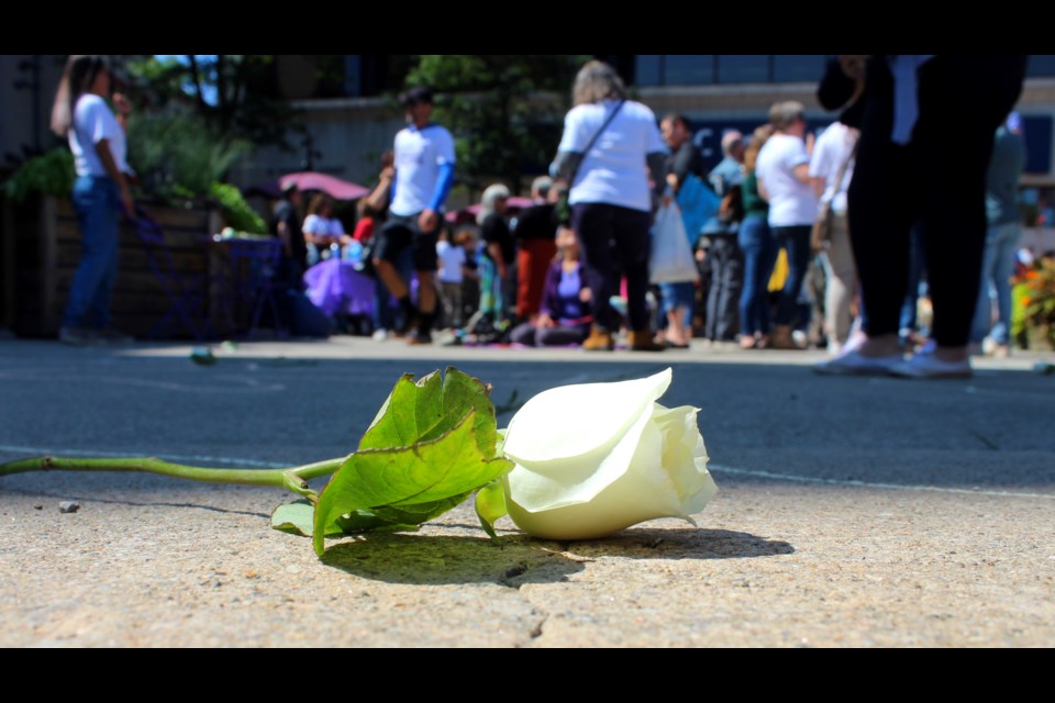 A white rose sits on the pavement at St. George's Square. It sits inside a chalked outline of a person who is honouring those who have died of a drug poisoning.