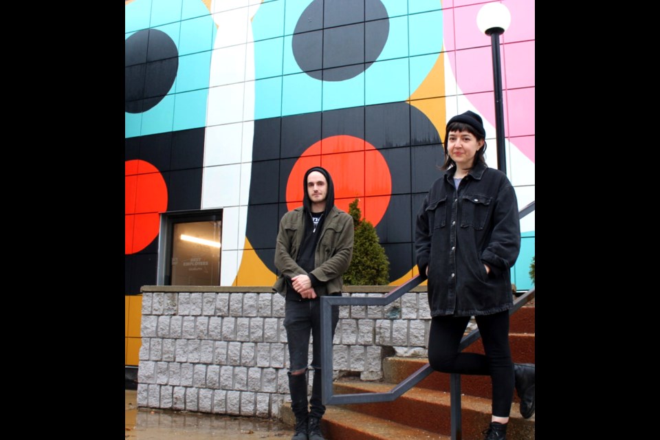 Gillian Wilson, right, and Quinn Henderson stand in front of an exterior mural painted on a former Holiday Inn on Scottsdale Drive. The building is being converted into a student residence.