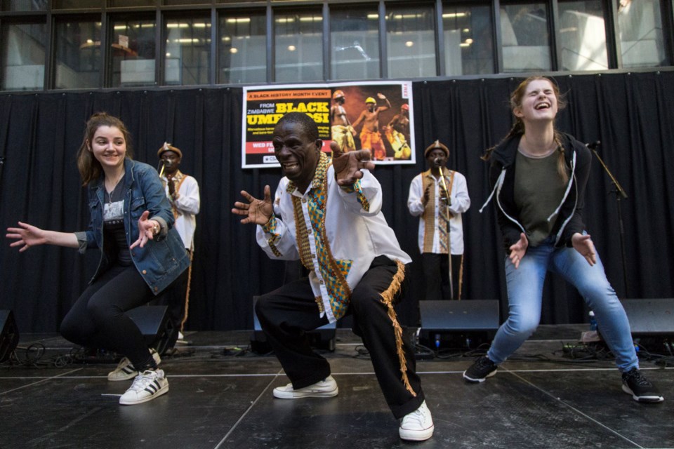 A member of Zimbabwe-based folk group Black Umfolosi leads GCVI students Kelly Falco (L) and Sarah Schmidt-McQuillan in a dance on stage during a show Wednesday at University Centre. Kenneth Armstrong/GuelphToday 