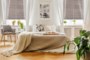 Open book on a gray, wooden armchair by a cozy bed with breakfast tray in a stylish bedroom interior with natural light coming through big windows