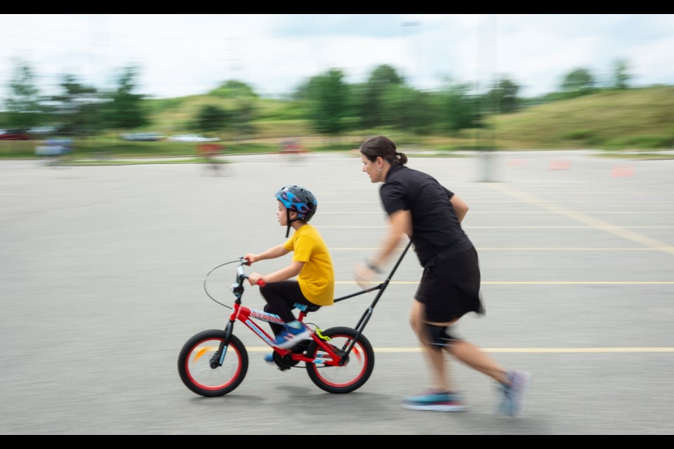 Jonny speeds on his new bicycle while being steadied by a volunteer during the KidsAbility I Can Bike camp held this week at the West End Community Centre. Kenneth Armstrong/GuelphToday