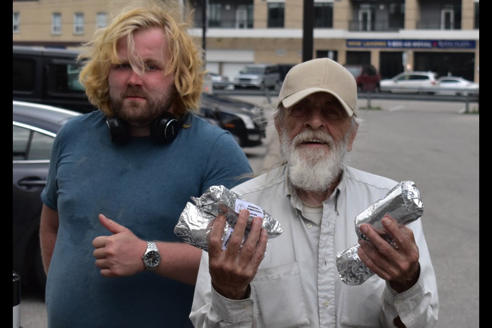 Brendan Bard (left) and Ed Pickersgill distribute
meals on July 13 at the bench, a weekly meetup spot where Kitchen Bees meals are brought to
after they are made. 