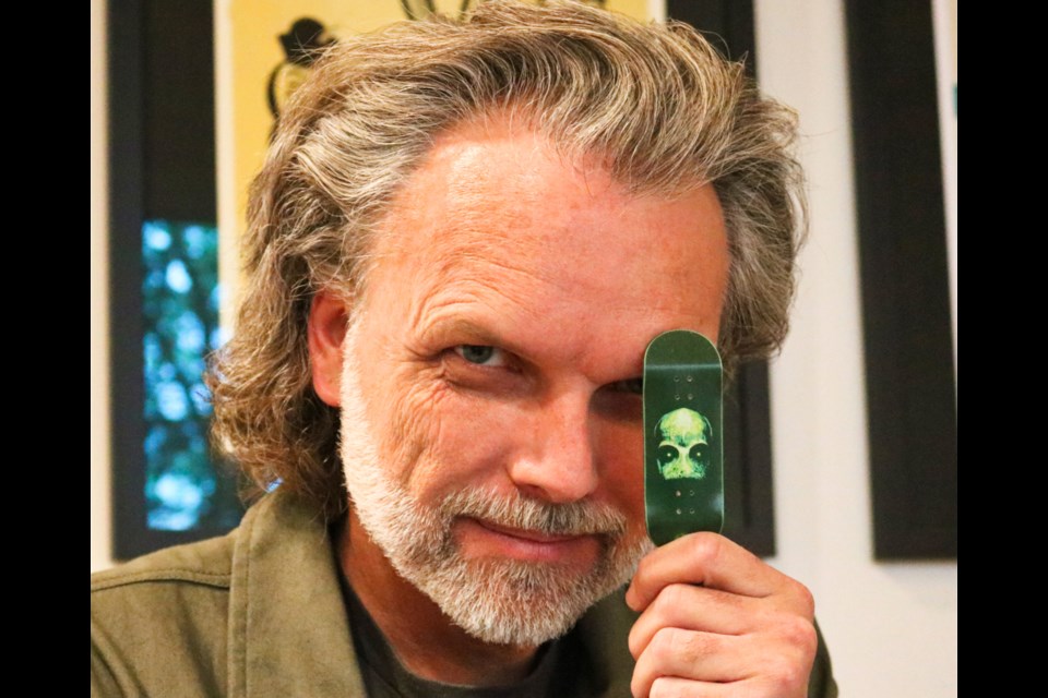 Keith Sheppard holds up a fingerboard deck with a photo of his sculpture on it.