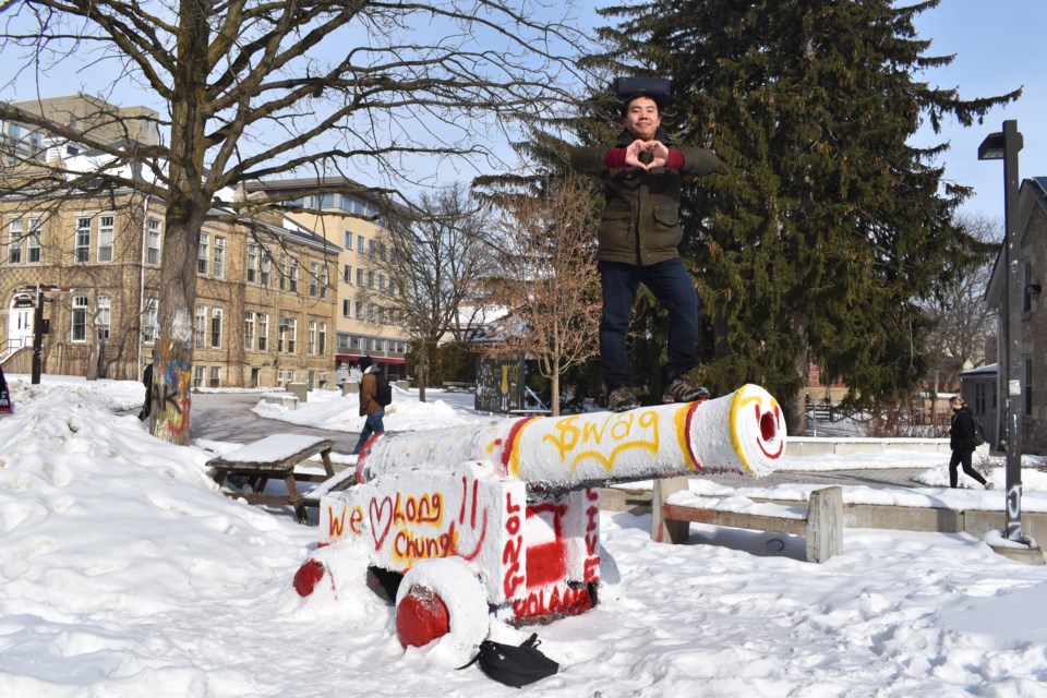 Long Chung balances his speaker on his head while posing beside the University of Guelph cannon painted in homage to him.