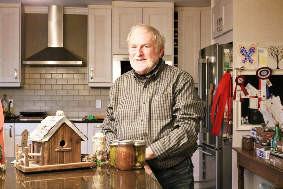 Rick Westgarth poses next to a bird house and canned goods he has made for county fair categories. Behind his shoulder, hangs ribbons he has won at past county fairs.