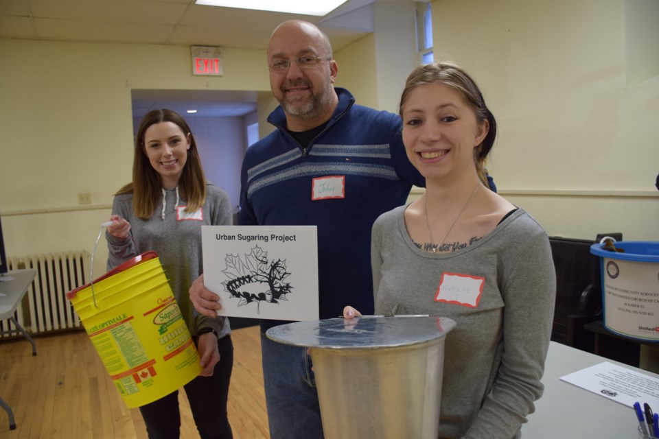 John Dennis with volunteers Kayla Goods, left, and Natalie Becker, were passing out the essential tools of maple tree tapping on Saturday, as Transition Guelph's Urban Sugaring Project gets rolling for the second year. Rob O'Flanagan/GuelphToday