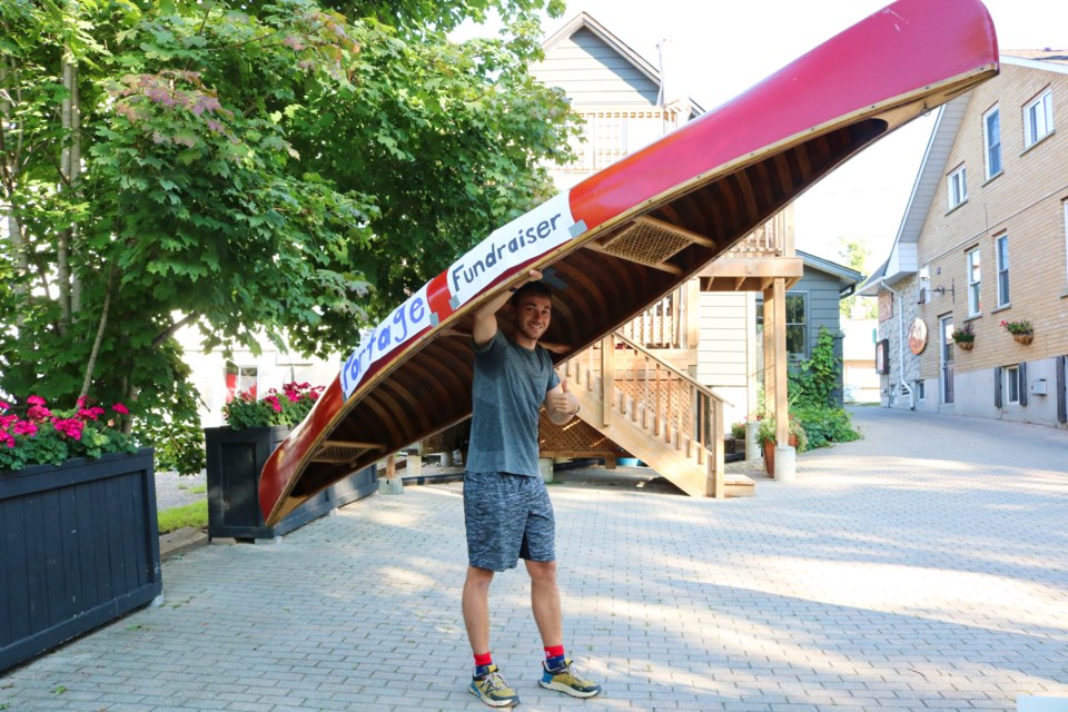 James Scott, owner of the Elora Paddle Company, posing under a red canoe before starting Portage for Portage. Ariel Deutschmann/GuelphToday