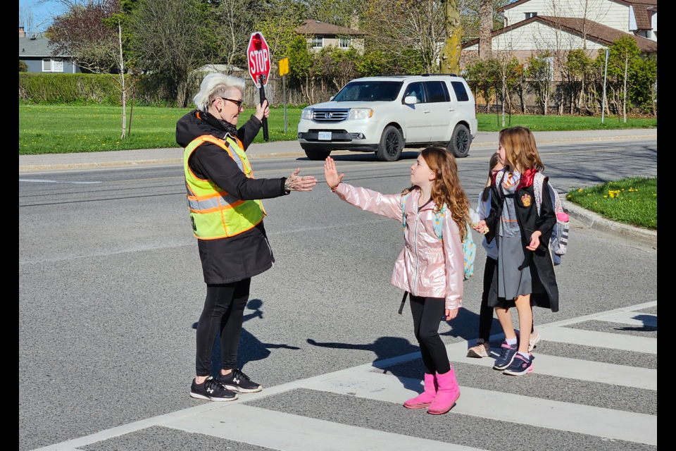 Barb Smith gives high fives to Sophia Reynolds (left) and Caidence Manes (right) as they cross Tanners Drive. The popular crossing guard is retiring after nine years helping students on their way to and from school.