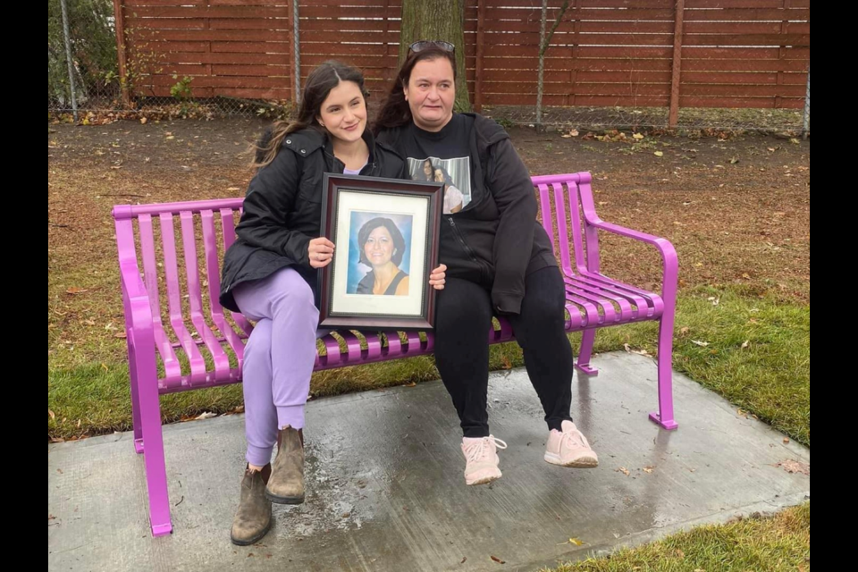 Sue Nesbitt-McNally's niece (left) Jenna Nesbitt and sister Laurie Nesbitt pose on the purple bench with a portrait of her.