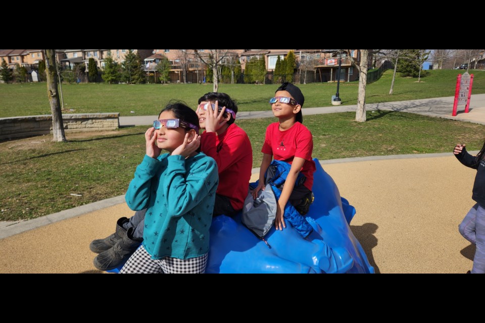 (Front to back) Nivedita and Vedant Nathroy and their friend Avyan Choubey paused their play at the Dominion Gardens Park to watch the eclipse.