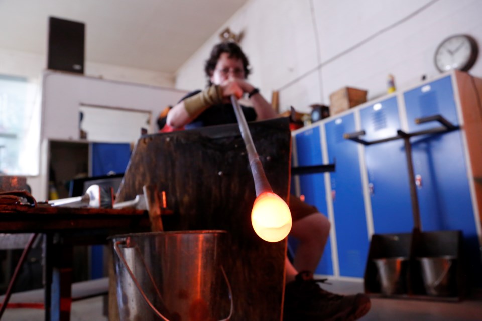 Skytree Smith blows into hot glass using her blow pipe. At this point, the glass is the consistency of taffy. 