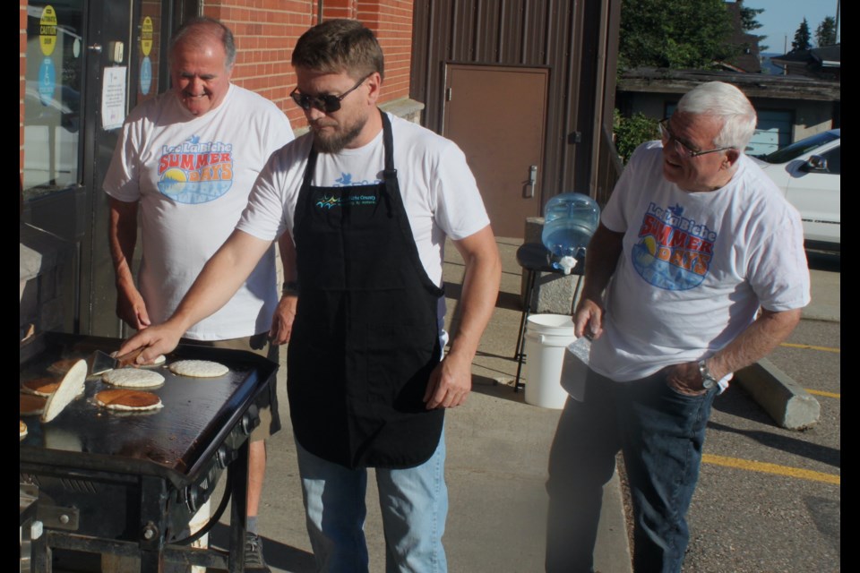 Former Lac La Biche mayors Aurel Langevin and Ovide Langevin look on as current mayor Paul Reutov flips pancakes for the breakfast that took place at the Lac La Biche Heritage Centre on Friday morning to start Summer Days. Chris McGarry photo.