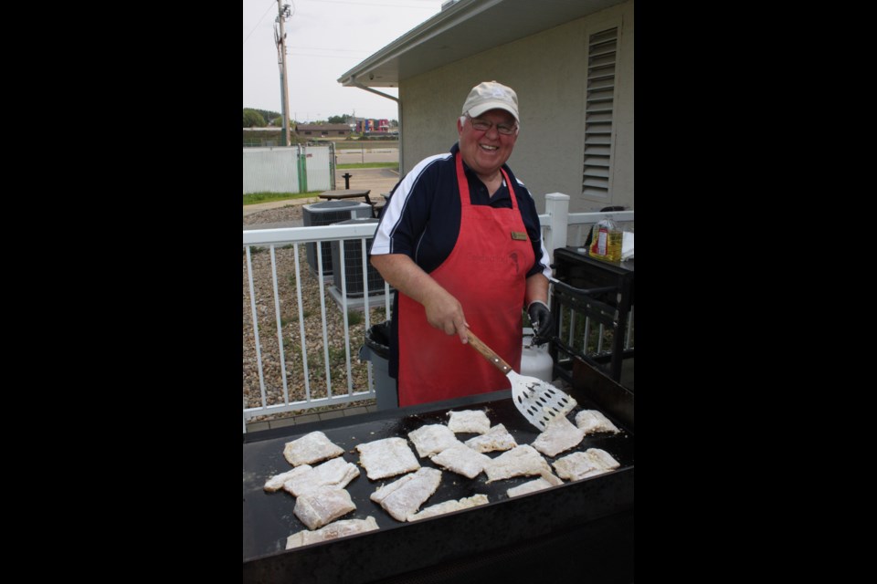 Cooking such an amount of fish is a tough job indeed, but Andy Gesner, a member of the Rotary Club of Lac La Biche, took it all with a smile as he flipped pieces of northern pike on the griddle as the community fish fry got underway Saturday evening. Chris McGarry photo.