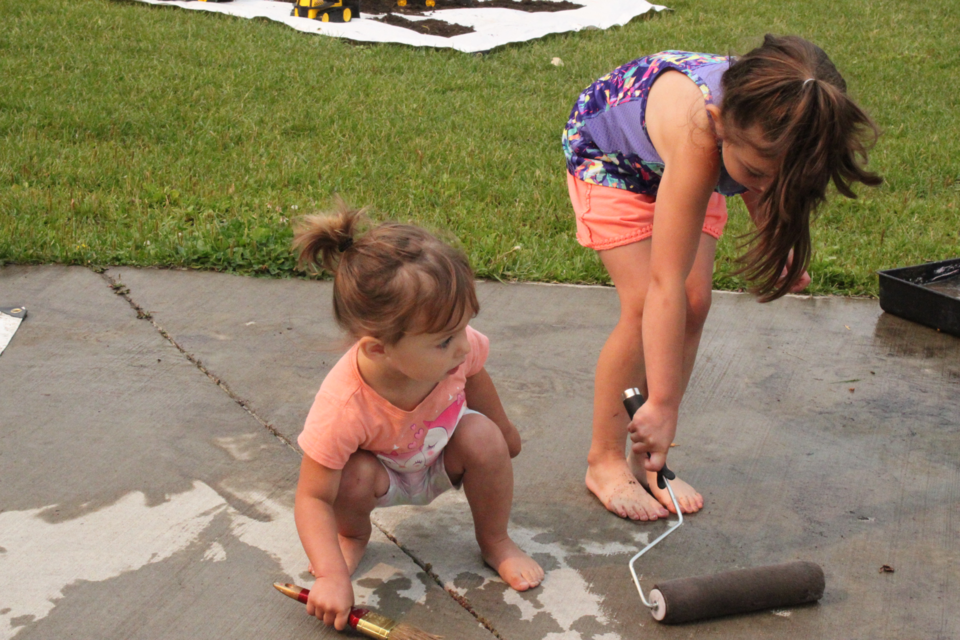 Hailey and Athena Burchill of Lac La Biche display their artistic talents by painting one of the walking paths at McArthur Park. Chris McGarry photo. 