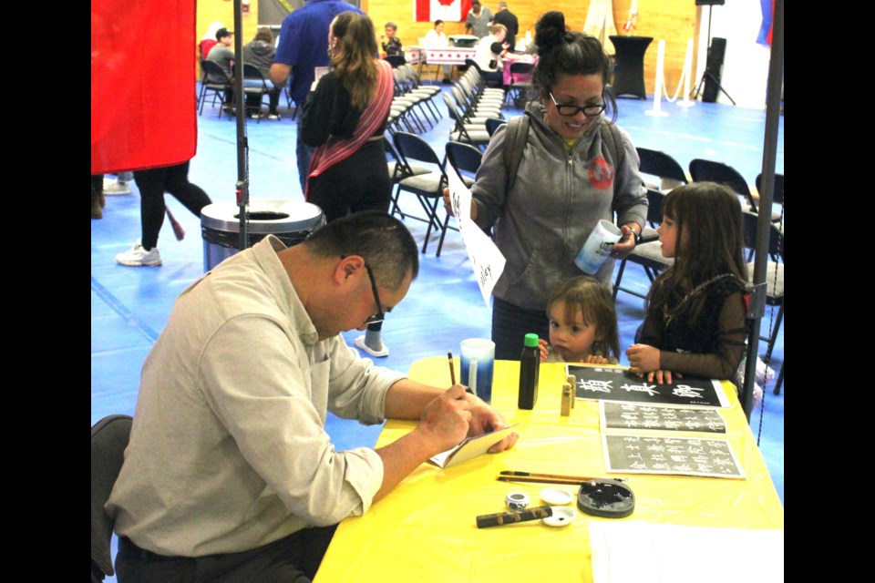 The artwork of the various cultures who’d made Lac La Biche County their home was also on display during the expo. Shun Li drew many people to his table as he instructed them how to do write calligraphy in traditional Chinese characters. Yesi Burchill and her daughters Hailey and Athena watch as Li does writes some calligraphy in the Chinese language. Chris McGarry photo. 