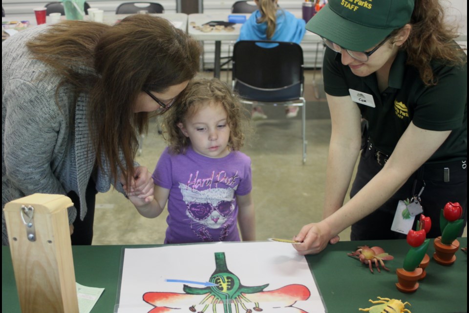 Cam Joduin, an interpreter at Sir Winston Churchill Provincial Park, teaches Lori Parenteau and her daughter, Cadence McKerlie, how pollination works by showing them how to play a game involving matching the names of flower parts to a large colourful flower that was part of an interactive display inside the campground ampitheatre at Sir Winston Churchill Provincial Park. The event, titled ‘Celebrating Pollinators and Art in the Park’, took place on Sunday, June 22. Chris McGarry photo. 