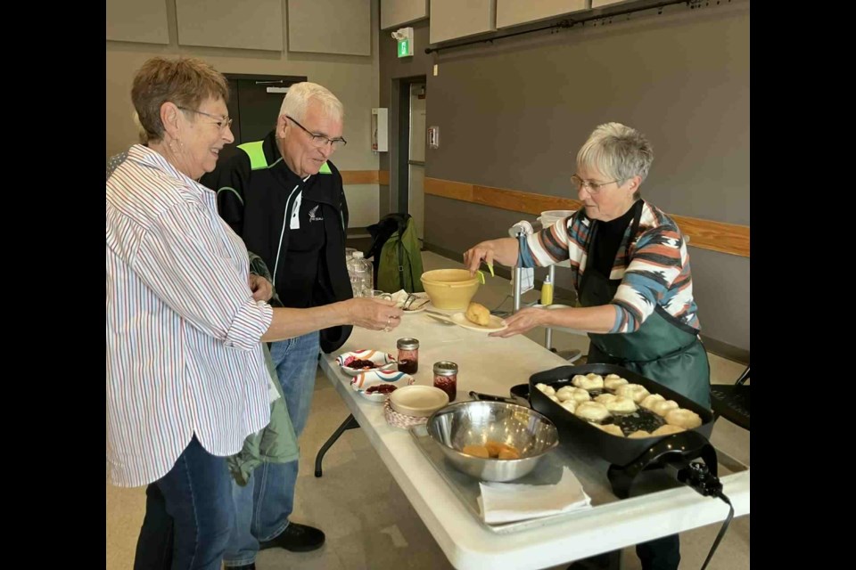 The 2025 Open Farm Days celebrations, which took place at the Lakeland Agricom on Aug. 16, featured, for the second year in a row, culinary demonstrations, including by put on by Donna Fabbro showing folks how to make fried Bannock. Fabbro gives some samples of freshly-made Bannock to Ovid and Donna Langevin. Chris McGarry photo. 