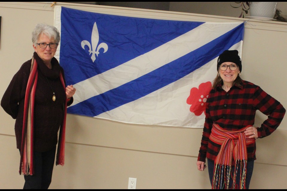 Geraldine Plamondon, left and her cousin, Crystal Plamondon, stand proudly on opposite sides of the Franco-Alberta flag, which was displayed prominently inside the Plamondon Festival Centre during the 2024 La Cabane å Sucre, which took place Sunday. Crystal Plamondon, who is a colourful traditional French-Canadian sash, is the cultural director for the ACFA Plamondon-Lac La Biche office, who puts on the event. Chris McGarry photo.