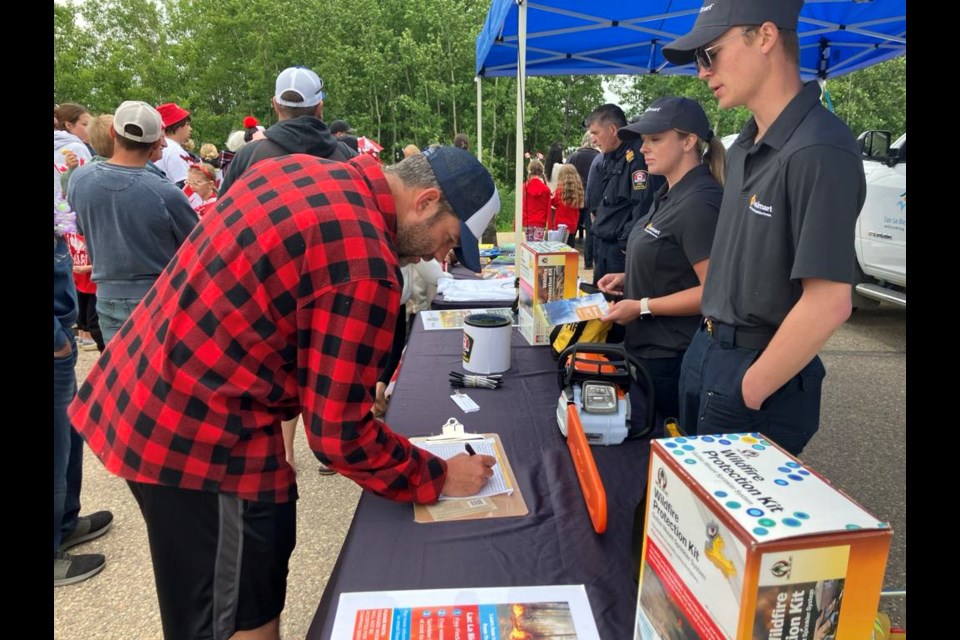 Ian Gagnon and Angelica Webb of FireSmart Alberta look on as Adam Brown fills out a form to have a FireSmart assessment done on his property. The event, which took place on June 28 in Lac La Biche County’s Mystic Beach subdivision to promote the FireSmart program, also included a free barbeque and a parade. Chris McGarry photo.