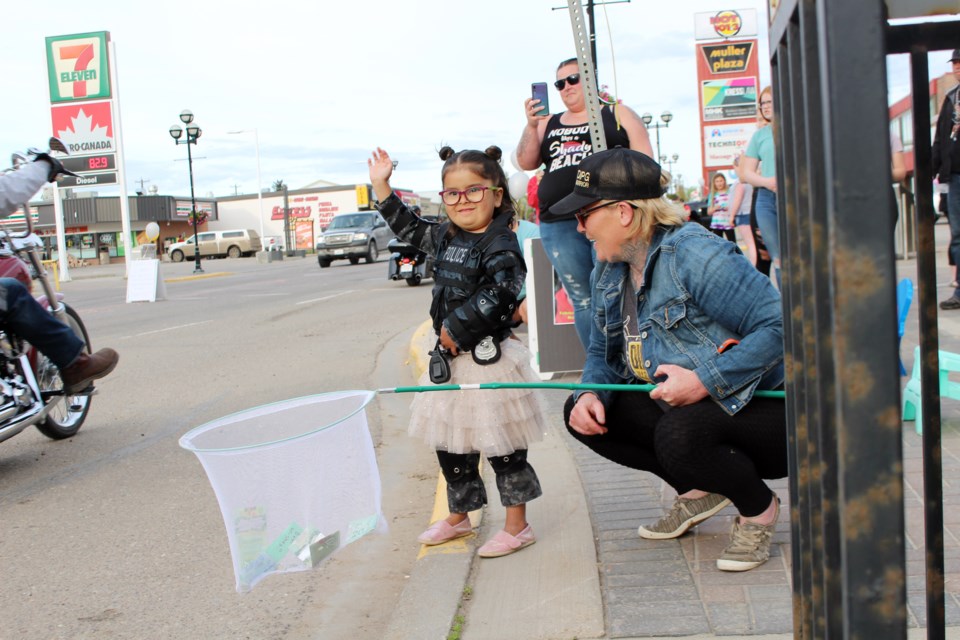 Princess Emma, 5, waves to cars and motorcycles driving down main street while her mom, Cathie Humphreys, holds her butterfly net on Thursday, May 28. Photo by Robynne Henry. 
