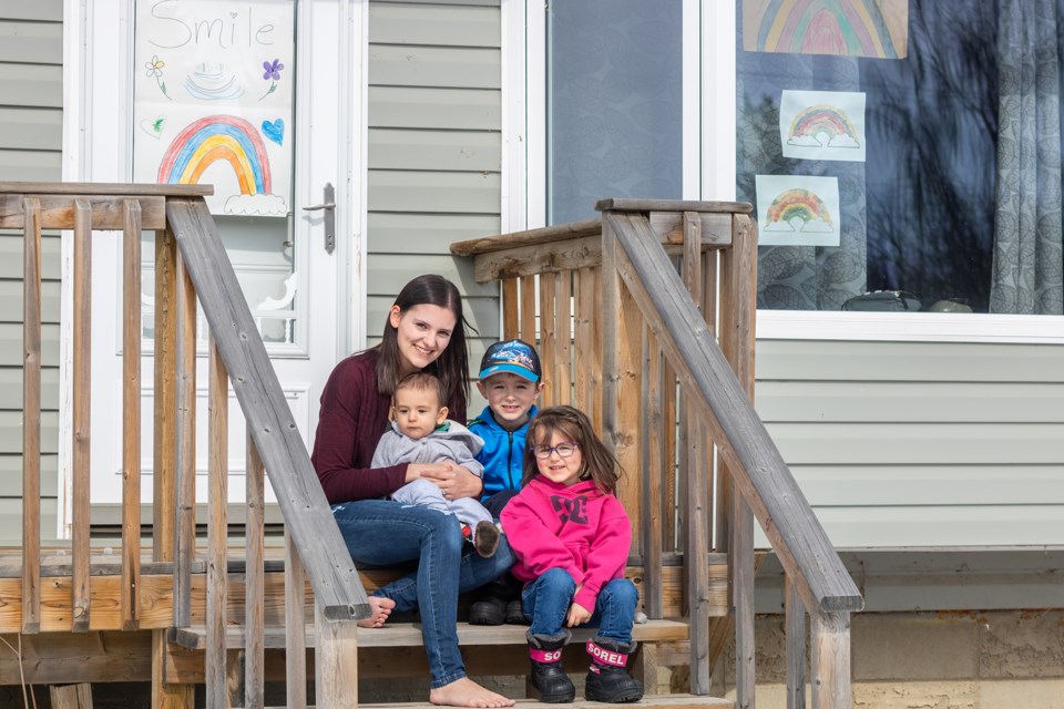 Bailey Mahé and her children, Kieran, Kyle and Adlee, sit in front of their home, where the windows have been decorated with fun artwork. Photo by Rushanthi Kesunathan